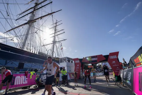 Runners looking tired after crossing the finish line at The Big Half, with landmark ship Cutty Sark in the background