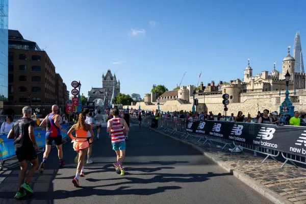 Runners running towards Tower Bridge in the background, blue skies and spectators cheering them on
