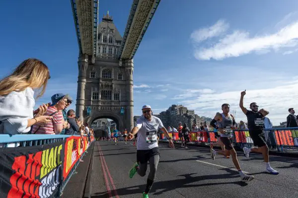 Runners crossing over Tower Bridge in London, smiling and pointing at the camera